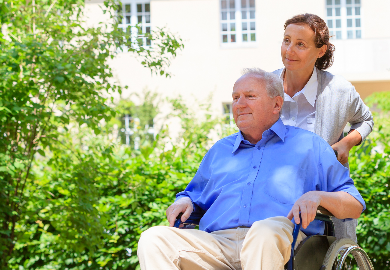 Woman pushing an elderly man in a wheelchair along a garden path.