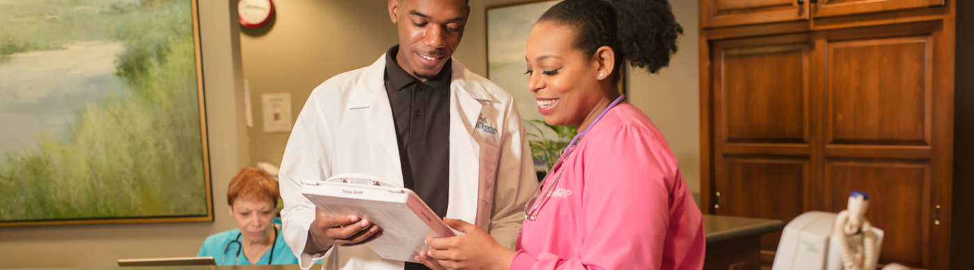 Two healthcare professionals, one in a white lab coat and the other in pink scrubs, discussing a clipboard.